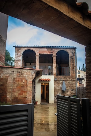 A courtyard with a stone building, a metal gate, and a door leading to an interior space. - Casa Camí de les Aigües (Monistrol de Montserrat)