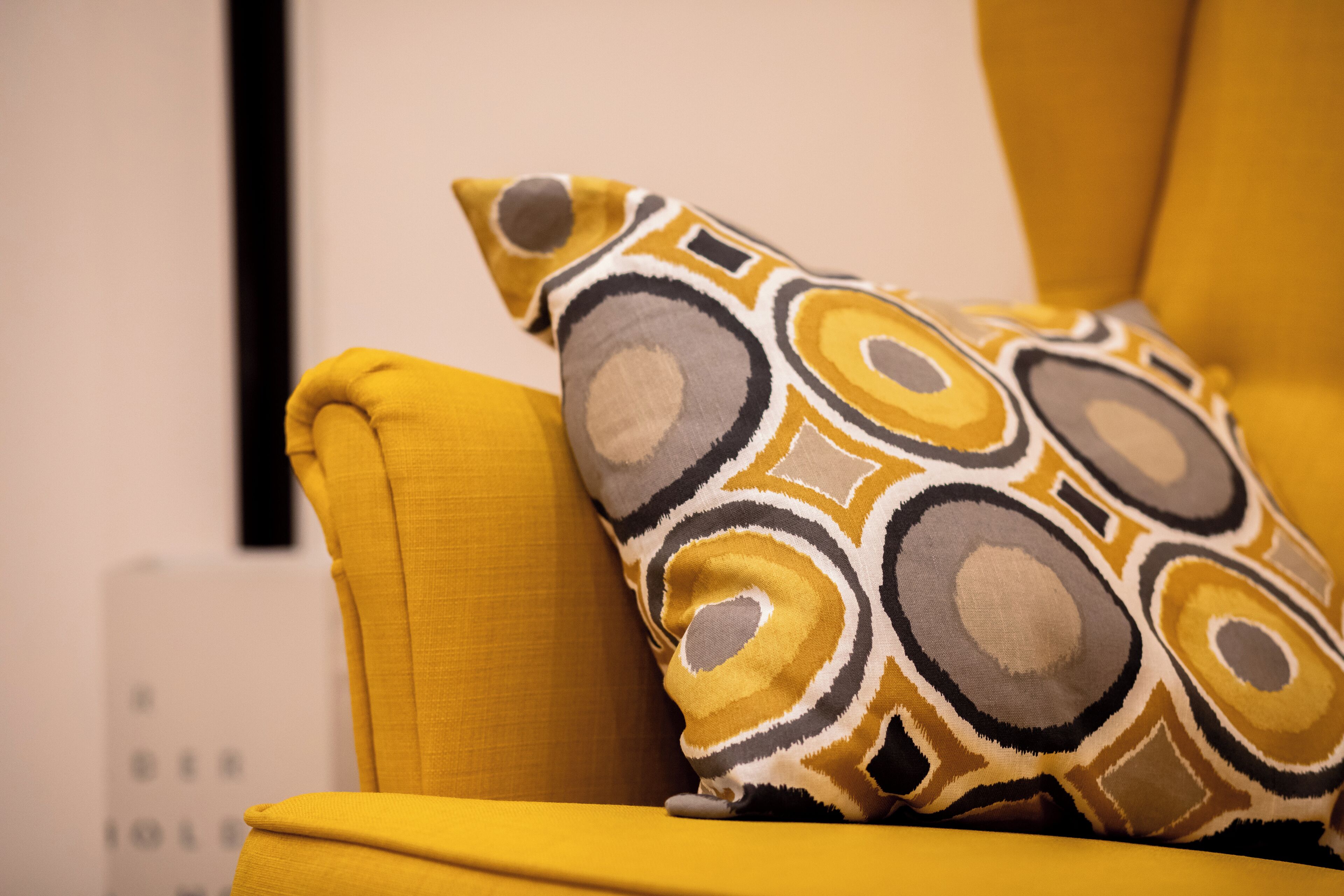 A yellow armchair with a patterned pillow.