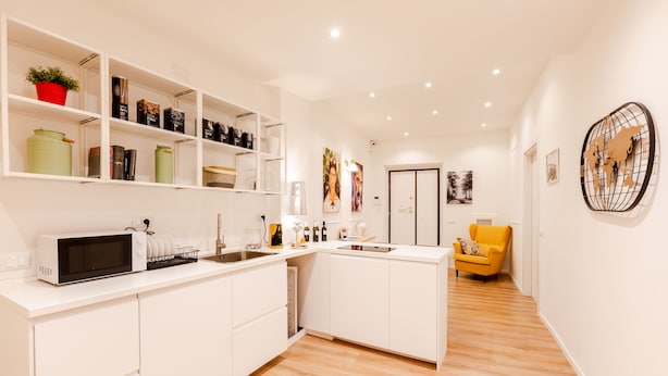A modern kitchen with white cabinetry, a microwave, and a sink. There are shelves with various items and a yellow chair in the background. - Rome Lux House guest rooms (Rome)