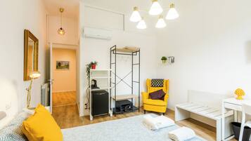 A compact, well-lit room with a bed, a yellow armchair, a small table, and a bunk bed.