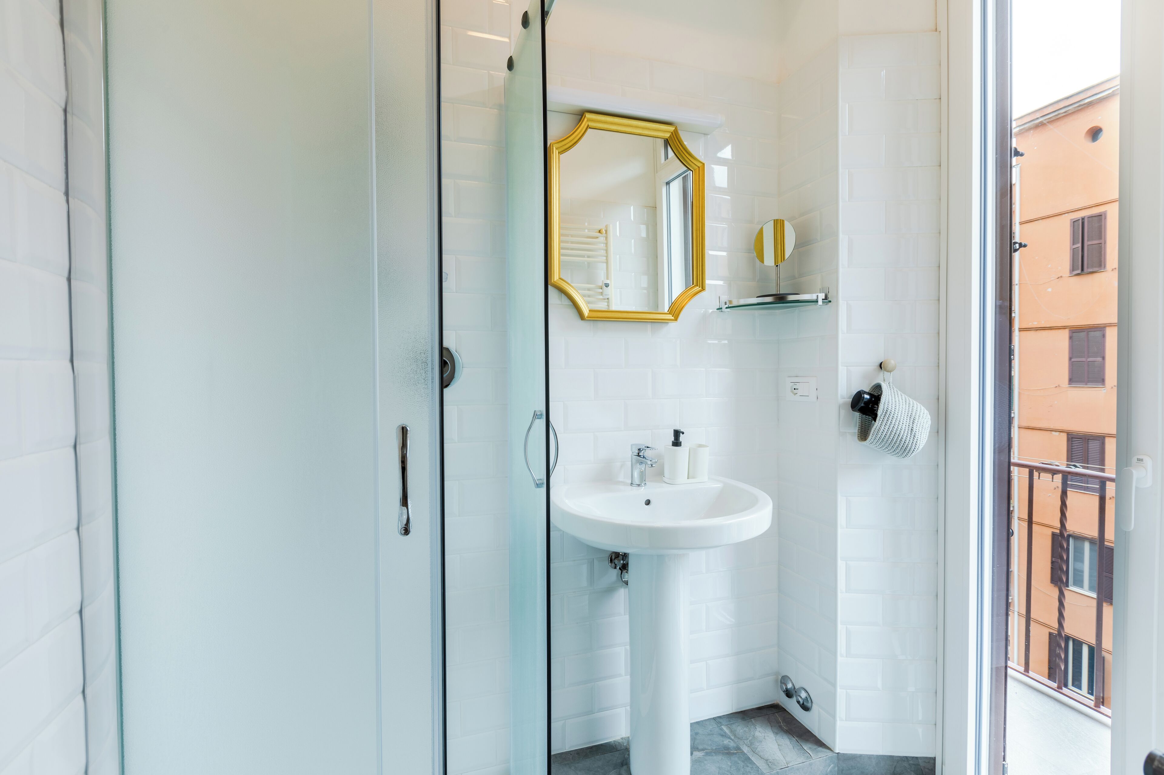 Une salle de bain moderne avec une douche à parois de verre, un lavabo blanc et un miroir encadré de doré.