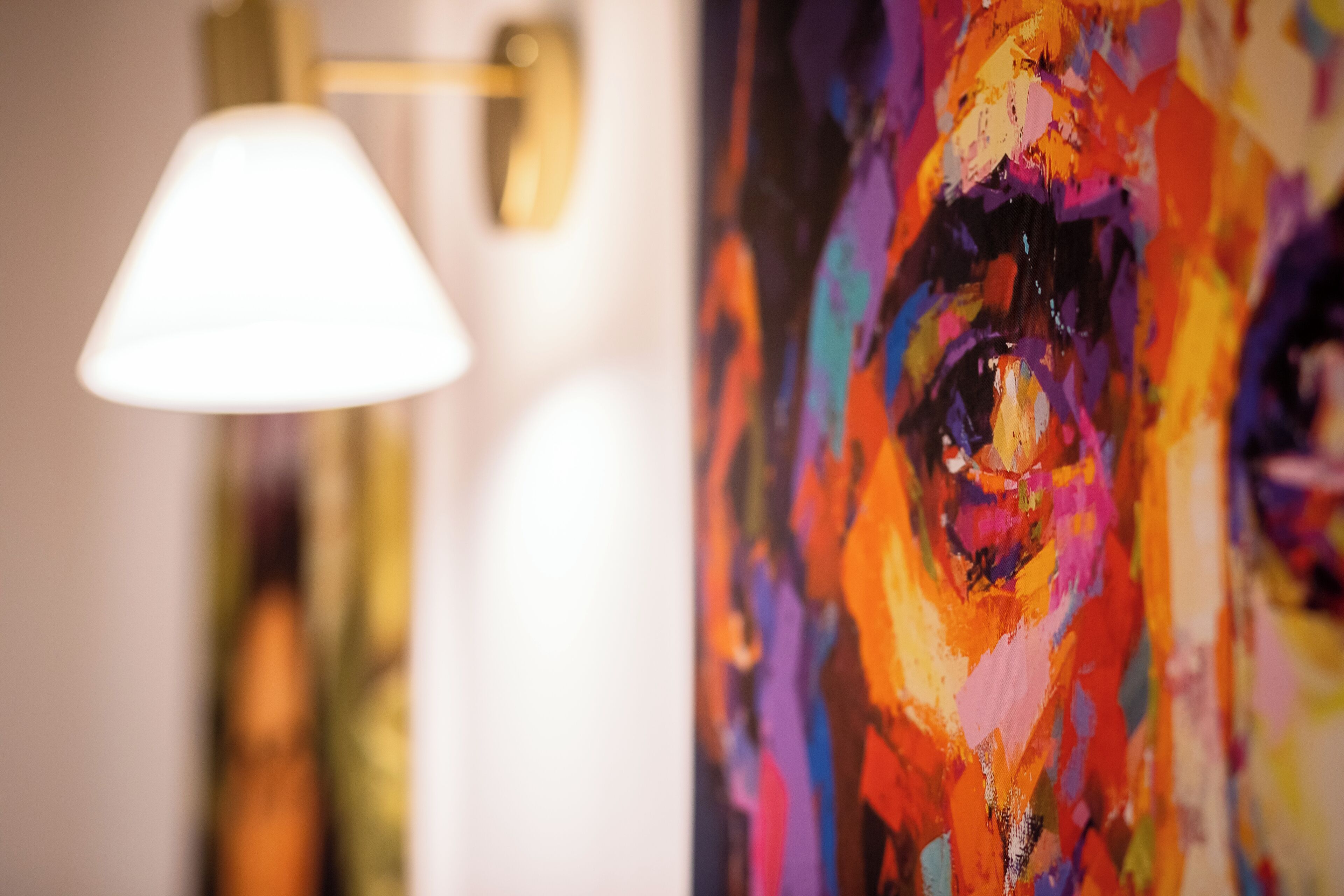 A close-up of a colorful abstract painting with a lamp in the background.