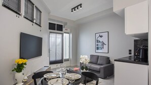 A modern living room with a flat-screen TV, a dining table set for four, a gray sofa, and a kitchen area with a coffee machine. - Sublime Studio Center of Paris Montmartre (Paris)
