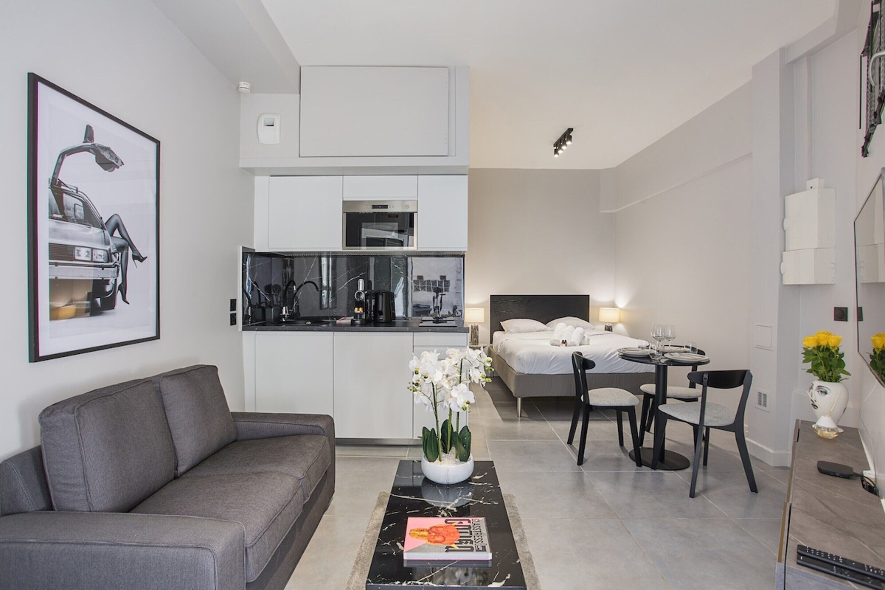 Un espacio habitable compacto con sofá, una mesa de comedor con sillas, cama y zona de cocina.