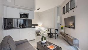 A modern living room with a sofa, a coffee table with a book, a dining area with a table and chairs, a kitchen with a microwave, and a TV mounted on the wall. - Sublime Studio Center of Paris Montmartre (Paris)