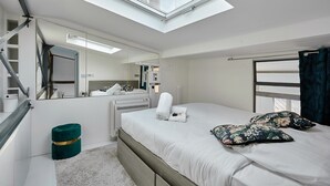 Una camera da letto moderna con un lucernario, un letto con cuscini a motivi floreali, un termosifone bianco e un poggiapiedi verde.
