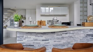 Una cucina moderna con isola a forma di ferro di cavallo, mobili bianchi e zoccolo in pietra.