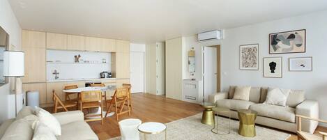 Uma sala de estar moderna com sofá, mesa de centro e cadeiras. Há uma área de cozinha com armários e uma mesa de jantar.