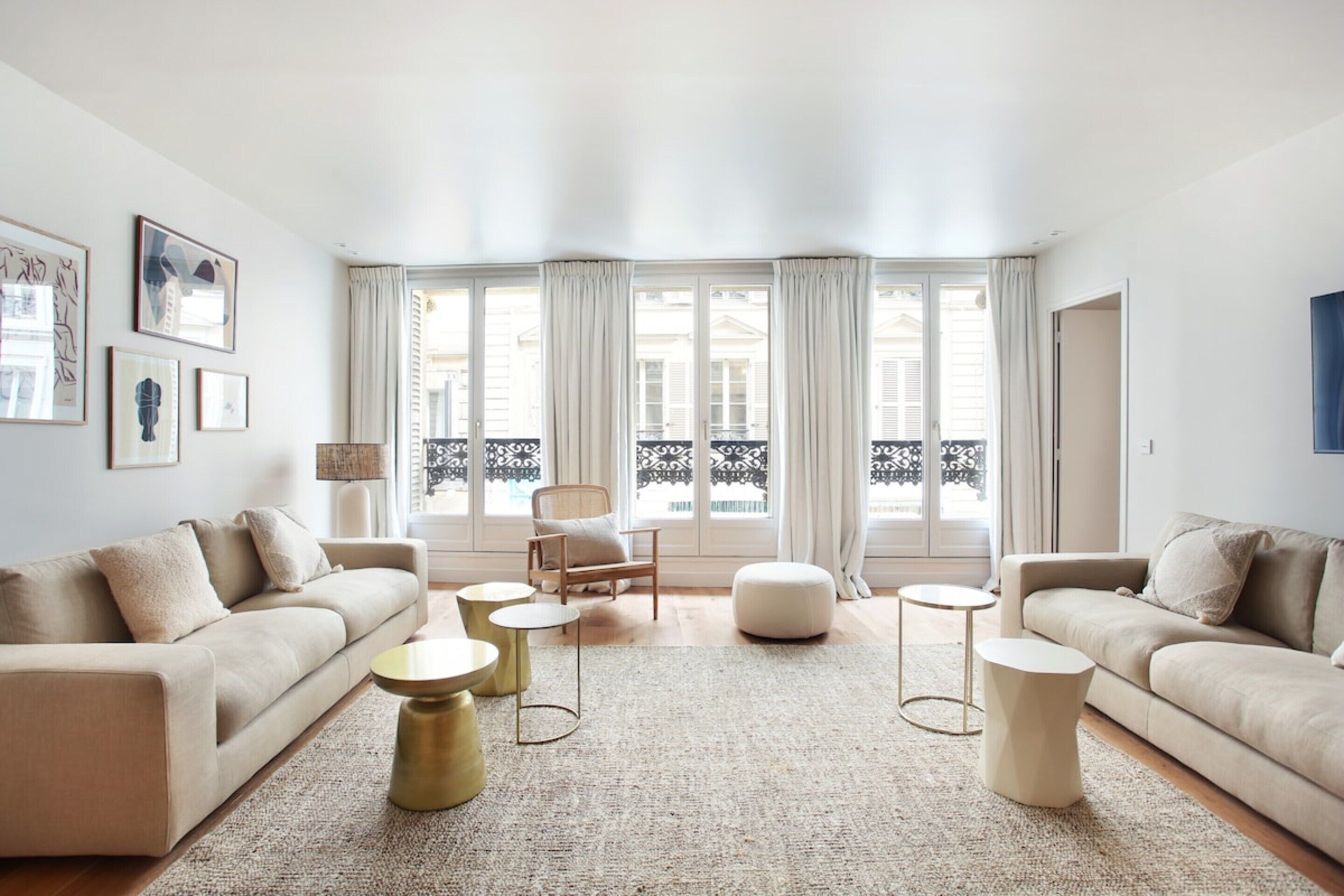 A spacious living room with a beige sofa set, a round coffee table, and a large window with curtains.