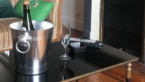 Un salon avec un canapé, une cheminée, une table sur laquelle se trouve une bouteille de champagne, un verre et une télécommande.