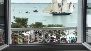 Un balcon donnant sur un port où l’on peut admirer des voiliers et un grand navire.