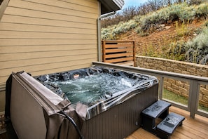 Un jacuzzi en una terraza de madera con un muro de piedra y vistas a una colina.