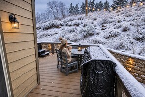 Une terrasse en bois avec un muret en pierre, des sièges d’extérieur et des guirlandes lumineuses.