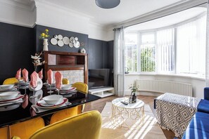 Relax in this stylish living room with a black accent wall, blue sofa, and a dining area featuring a black table and yellow chairs.