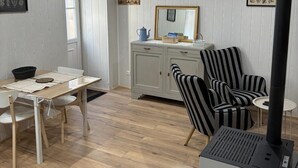 Een kamer met een eettafel, stoelen, een kast, een gestreepte fauteuil, een bijzettafeltje en een zwarte verwarming.