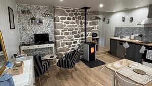 Een moderne keuken met een accentmuur van steen, een ingebouwde kookplaat en een eethoek met een houten tafel en gestreepte stoelen.