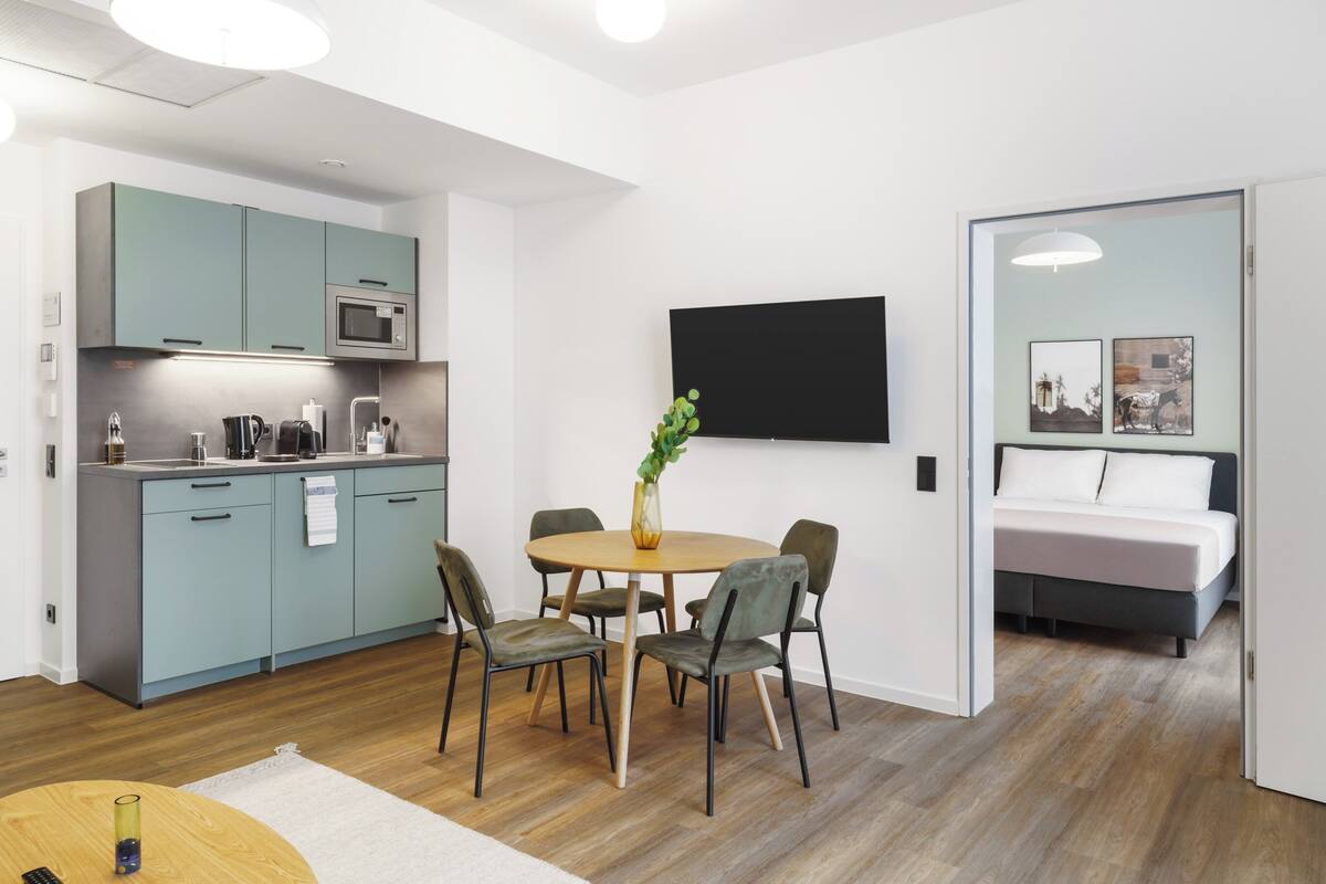 A modern hotel room with a kitchen, a dining area, and a bedroom.