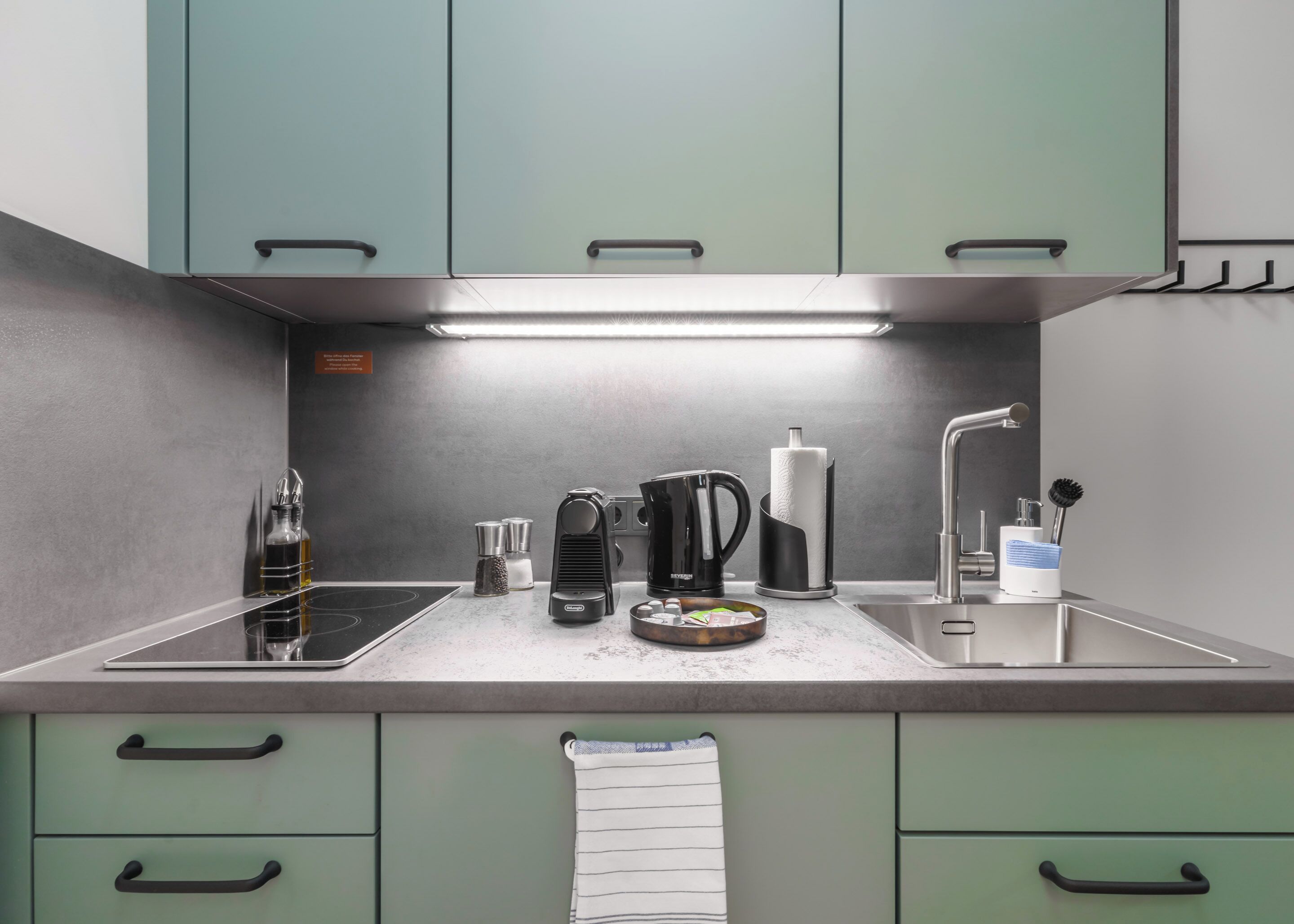 A modern kitchen with a built-in stove, a coffee maker, a kettle, and a sink.