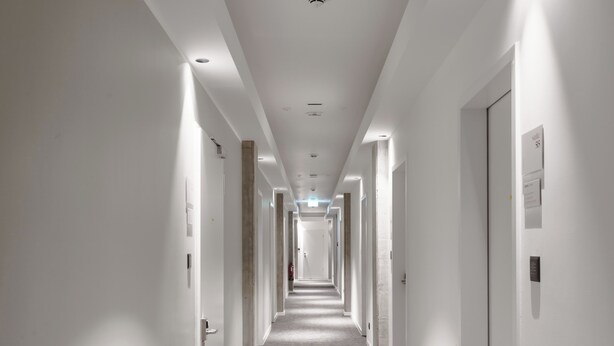 A long, narrow hotel corridor with white walls and doors on both sides. - Limehome Berlin Sybelstraße (Berlin)