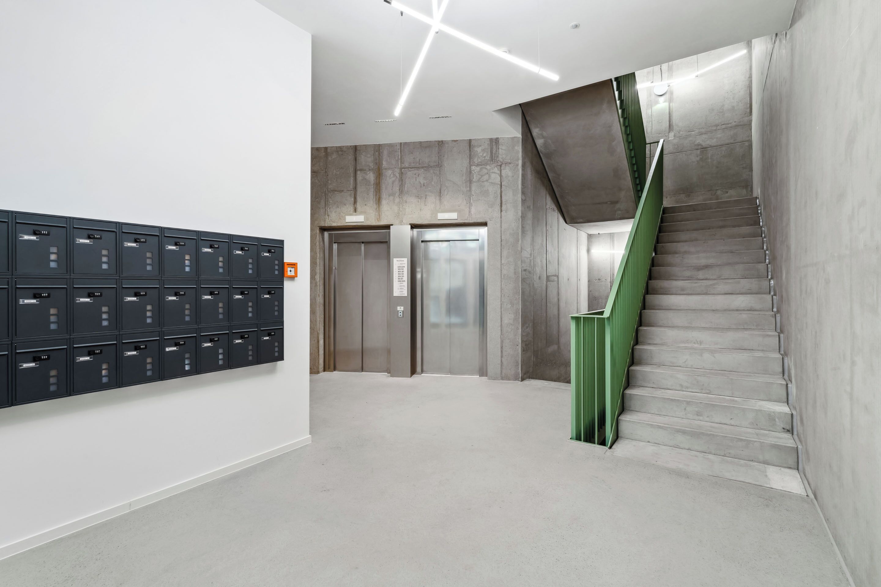 A modern interior with a staircase, elevator, and a row of lockers.