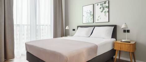 Un dormitorio moderno con una cama grande, una mesita de noche con lámpara y dos impresiones botánicas enmarcadas en la pared.