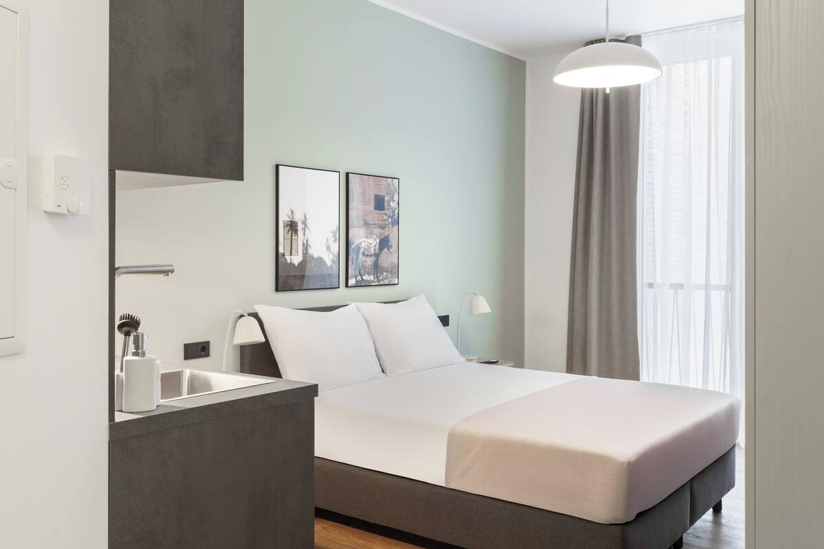 A modern hotel room with a large bed, a bedside table, a mirror, and a window with curtains.