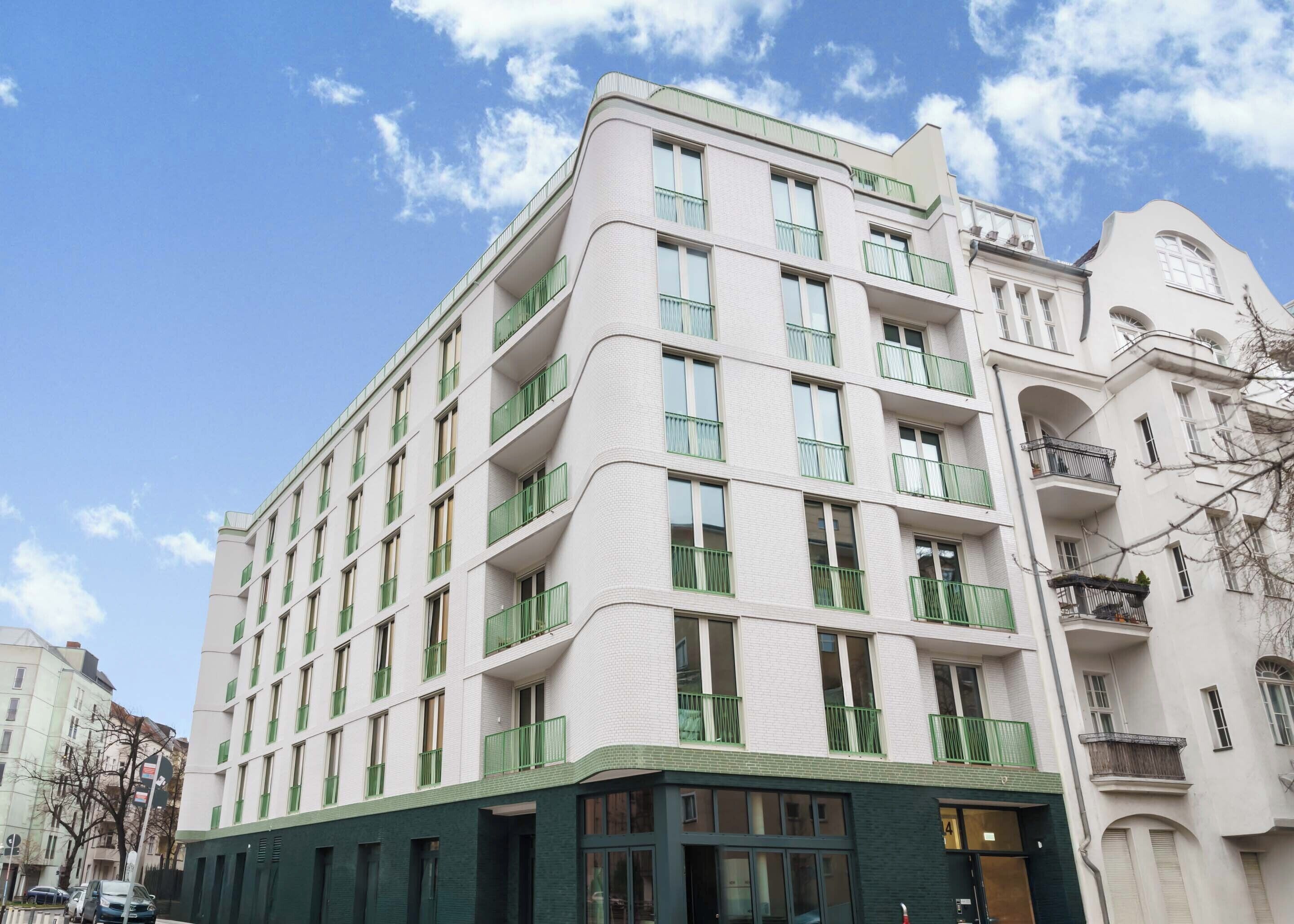 A multi-story hotel with a white facade, green balconies, and a green lower section.