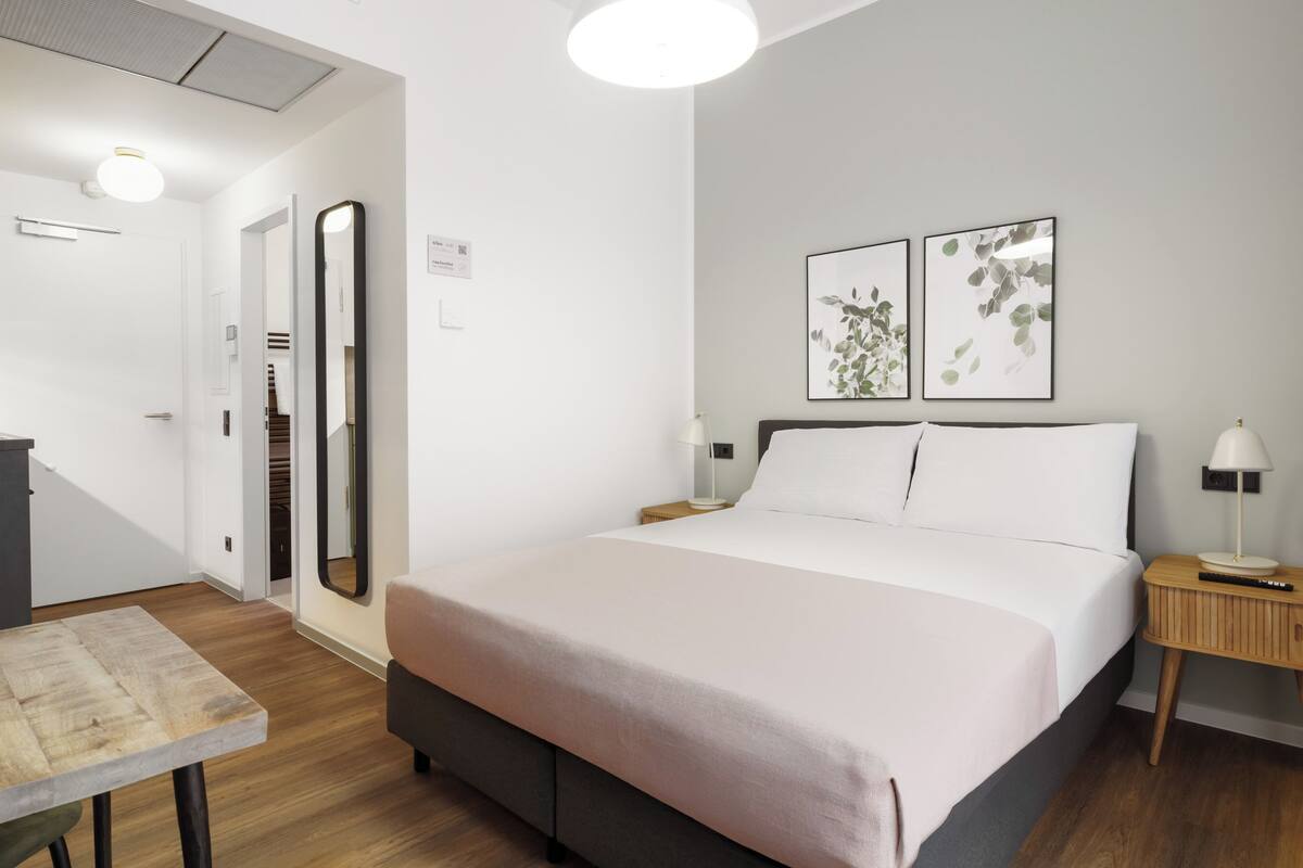 A modern bedroom with a bed, bedside tables, a desk, and a mirror.