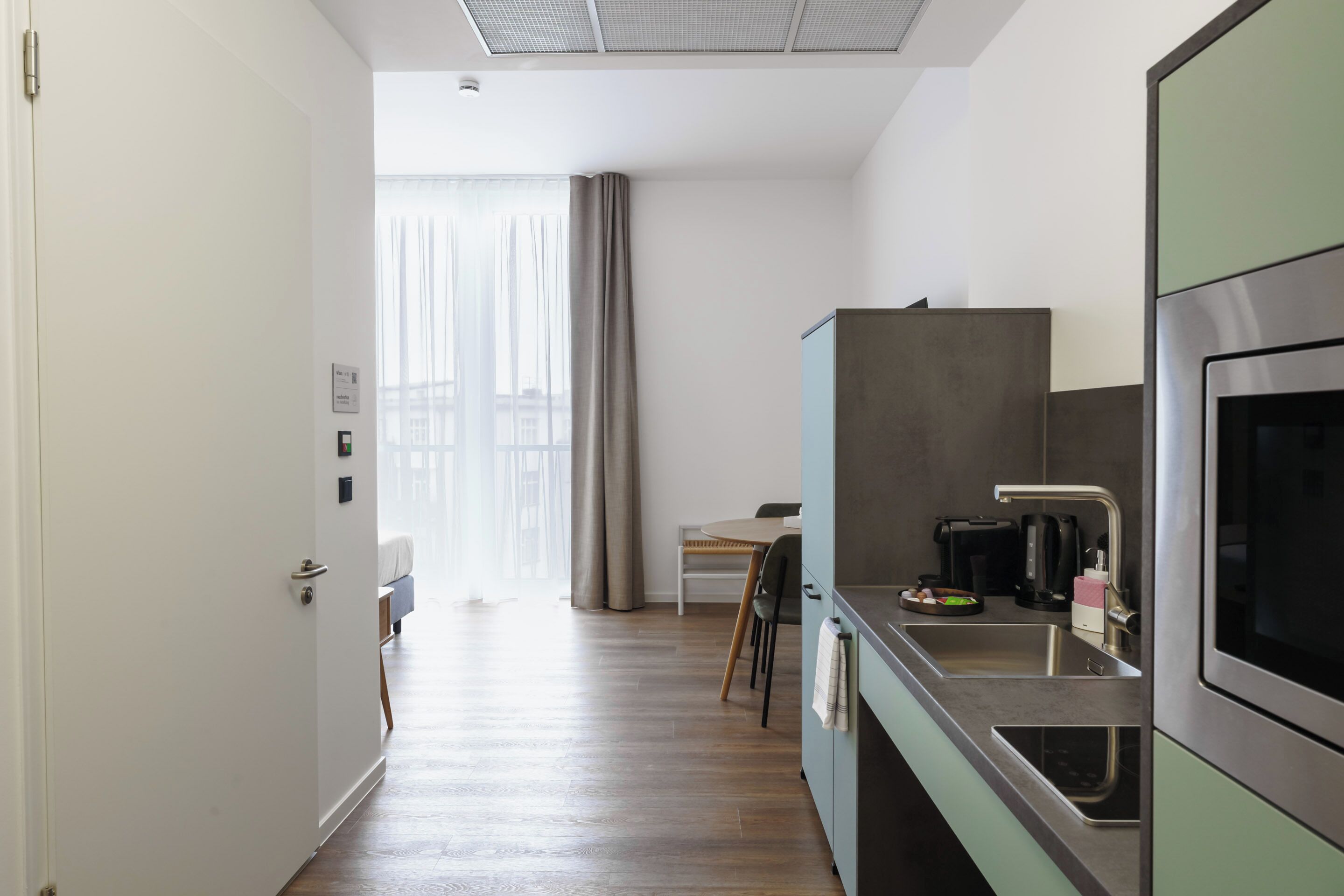 A modern kitchen with a stainless steel sink, a built-in oven, and a dining area with a table and chairs.