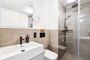 A modern bathroom with a white sink, a toilet, and a glass-enclosed shower area. - Limehome Berlin Sybelstraße (Berlin)