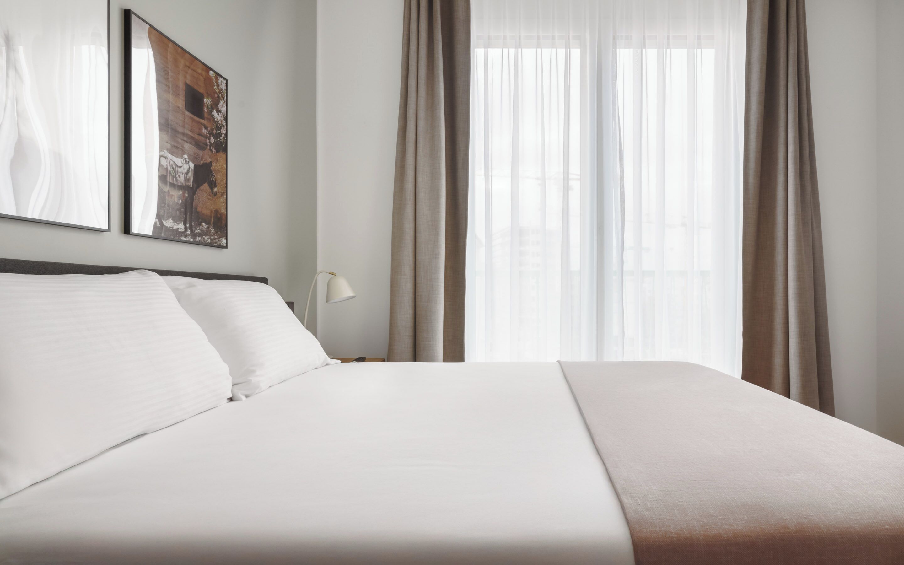 A neatly made bed with white linens, a bedside lamp, and a framed picture on the wall.