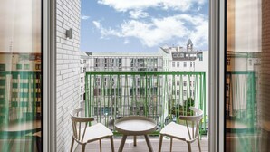 A balcony with a table and chairs, a green metal fence, and a view of buildings in the background. - Limehome Berlin Sybelstraße (Berlin)
