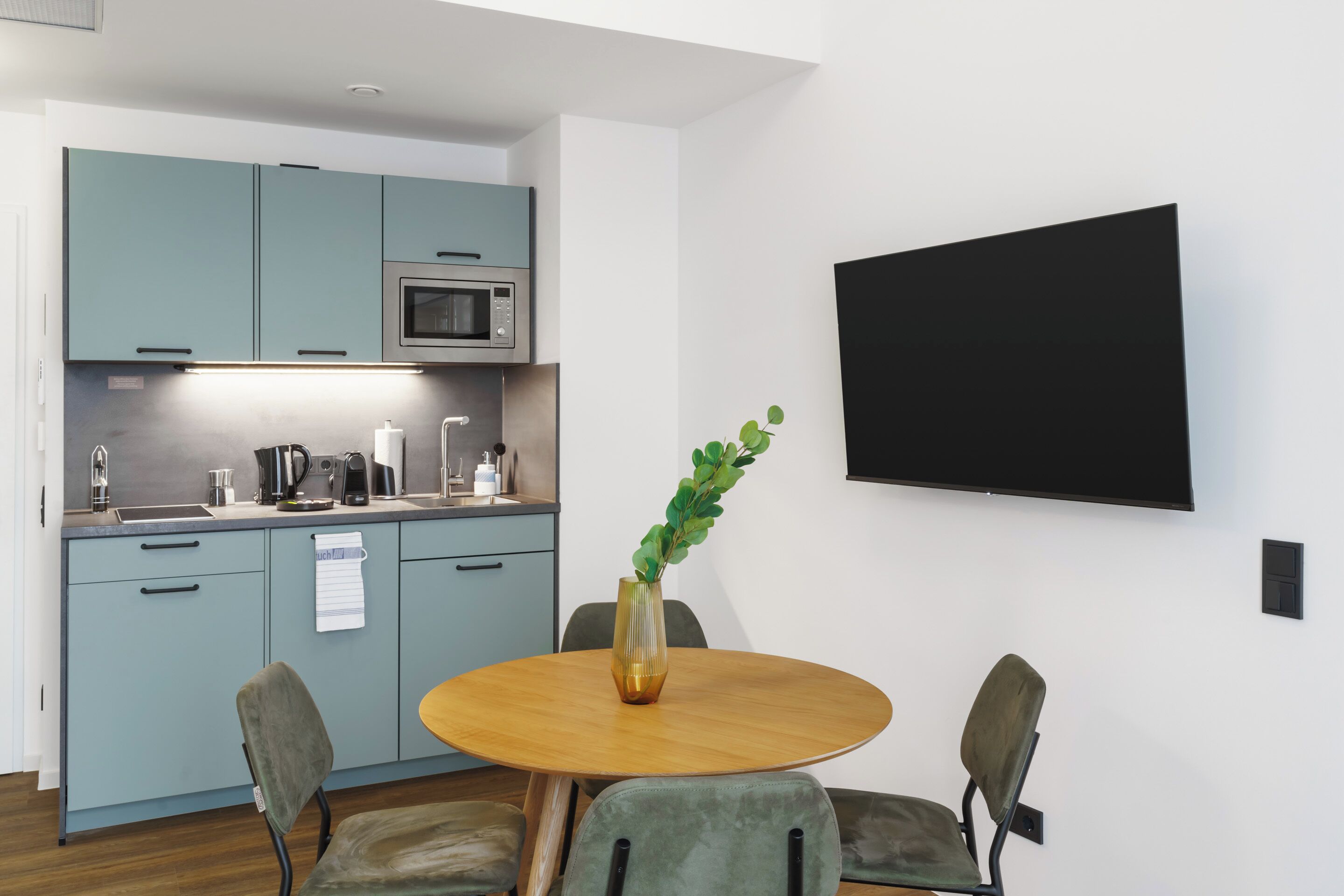Una cucina moderna con mobili color petrolio, un forno a microonde e un'area pranzo con un tavolo rotondo e sedie.