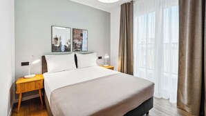 A hotel room with a large bed, two bedside tables with lamps, a ceiling light, and a large window with curtains. - Limehome Berlin Sybelstraße (Berlin)