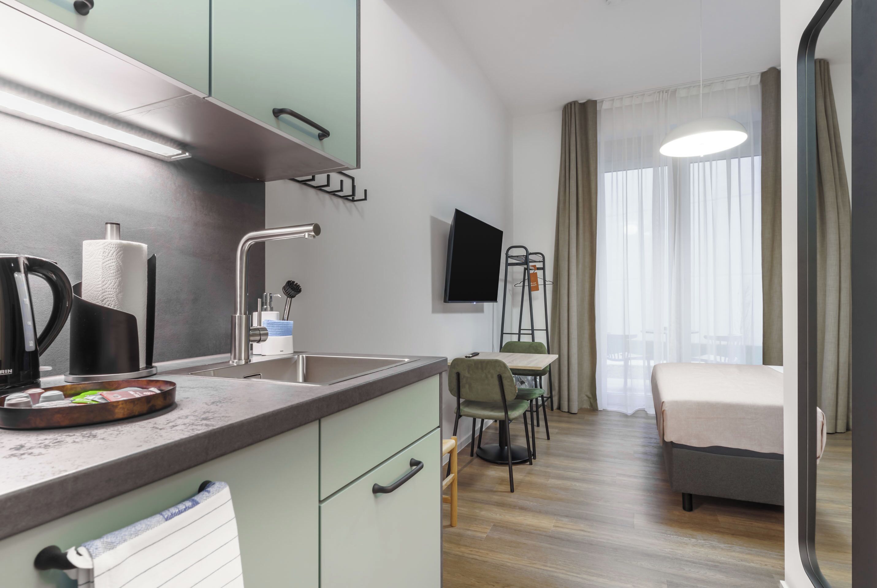 A modern hotel room with a kitchen area, a dining table, and a bed.