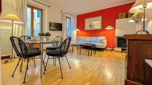 A modern living room with a red accent wall, a white sofa, and a dining area with a glass table and black chairs. - RED81 Suite - 10 min dal Duomo - 2 camere (Milan)
