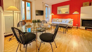 A living room with a round glass table, two black chairs, a white sofa, and a red accent wall. - RED81 Suite - 10 min dal Duomo - 2 camere (Milan)