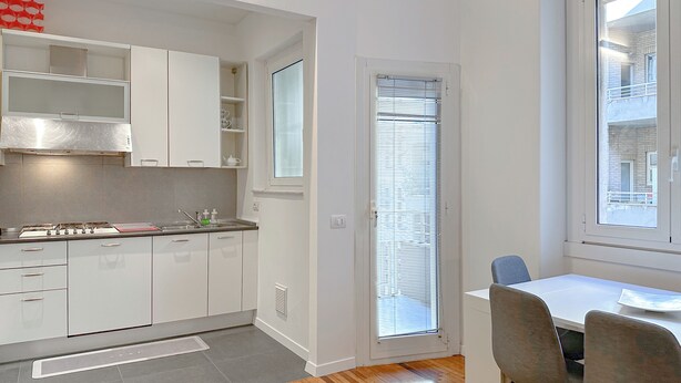 Una cocina moderna con armarios blancos, estufa integrada y una ventana con persianas.