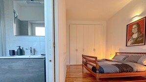 Un dormitorio con una cama de madera, un armario blanco y un baño con espejo y lavamanos.