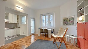 Una cocina moderna con armarios blancos, un comedor con mesa y sillas, y un mueble rojo con estantes.