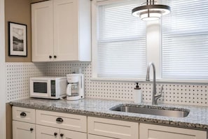 A kitchen with white cabinets, a granite countertop, a stainless steel sink, a microwave, and a coffee maker. - Near UD! Just 2.4 miles from Campus. Snug & Stylish With Fenced In Yard (Dayton)