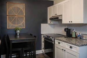 A kitchen with white cabinets, a black stove, and a coffee maker on the counter.