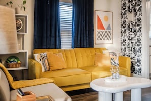 A living room with a mustard yellow sofa, a white coffee table, and a blue curtain.