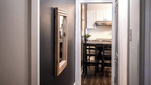 Un pasillo que conduce a una cocina con un espejo de marco de madera en la pared, una mesa de comedor y sillas.