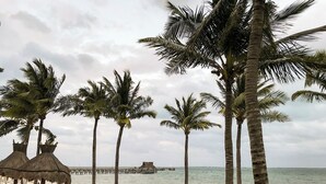 A beach with palm trees, a thatched-roof structure, and lounge chairs along the shore.