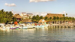 A marina with several boats docked, a thatched-roof building, and palm trees in the background.