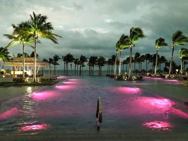 A pool area with palm trees and a gazebo, surrounded by a beach view.