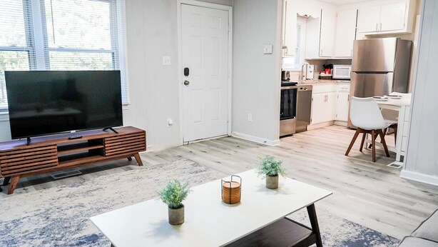 A modern living room with a flat-screen TV, wooden entertainment unit, and a dining table with potted plants.
