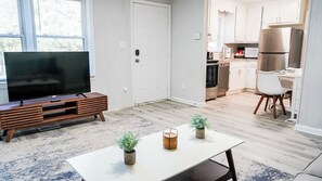 A modern living room with a flat-screen TV, wooden entertainment unit, and a dining table with potted plants. - Cozy Escape Just Minutes from Duke & Dwntwn Durham (Durham)
