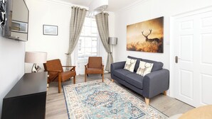 A living room with a sofa, chairs, a TV, a rug, and a painting of a deer. - Argyl | Charming 2-Bedroom Apt. on Thistle Street (Edinburgh)